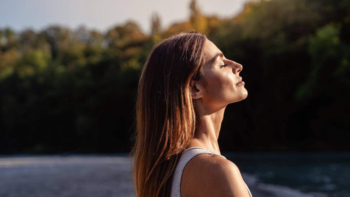 woman outside looking at peace slightly smiling facing the sun with her eyes closed